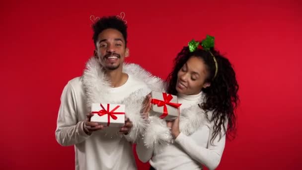 Young african american couple with christmas gift box dancing isolated on red background studio. New 2020 year decorations, presents, party, happiness concept. - Video