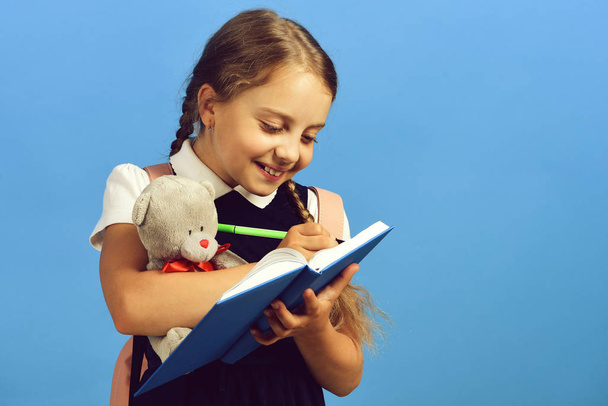 Girl holds teddy bear and writes in blue notebook - Foto, immagini