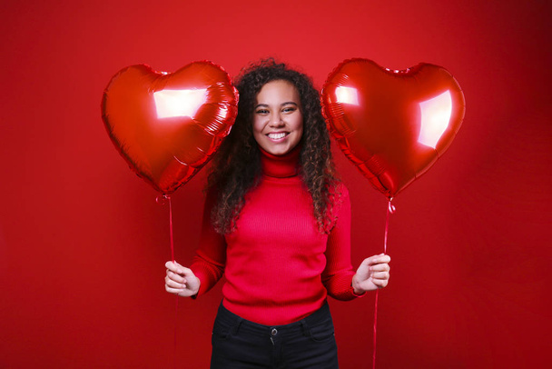 Gorgeous young woman posing over red wall holding helium inflated balloon. - Фото, зображення