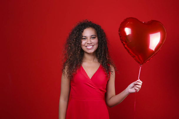 Gorgeous young woman posing over red wall holding helium inflated balloon. - Foto, Bild