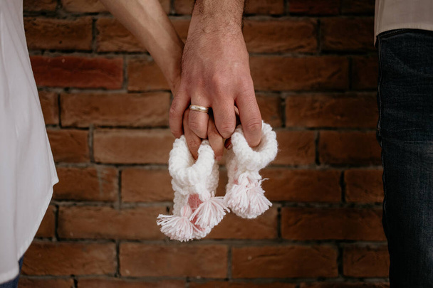 Νεαρό ζευγάρι περιμένει το μωρό κρατώντας μικρές άσπρες κάλτσες μπροστά από κόκκινα τούβλα - Φωτογραφία, εικόνα