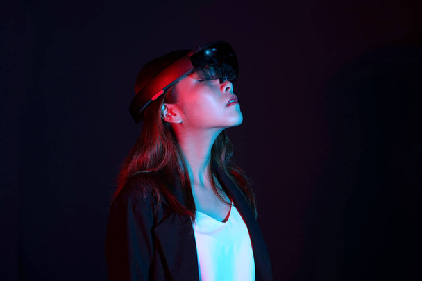 Μια επιχειρηματίας δοκιμάζει ολογράφους γυαλιών στο σκοτεινό δωμάτιο. Πορτρέτο της νεαρής ασιατικής κορίτσι εμπειρία ar. Μελλοντική τεχνολογία και δύναμη της έννοιας του φεμινισμού - Φωτογραφία, εικόνα