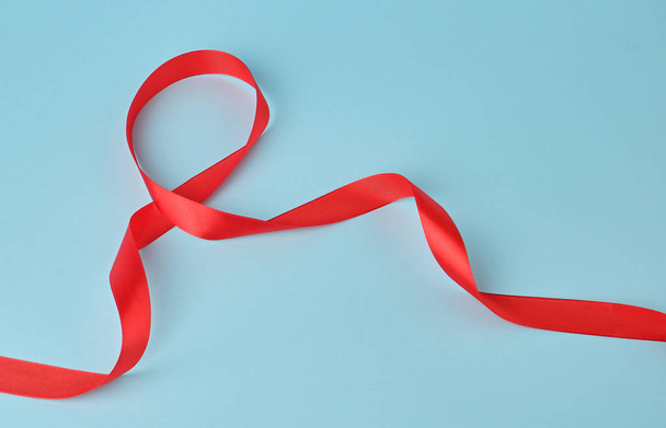 cinta delgada de seda roja retorcida sobre un fondo azul
 - Foto, imagen