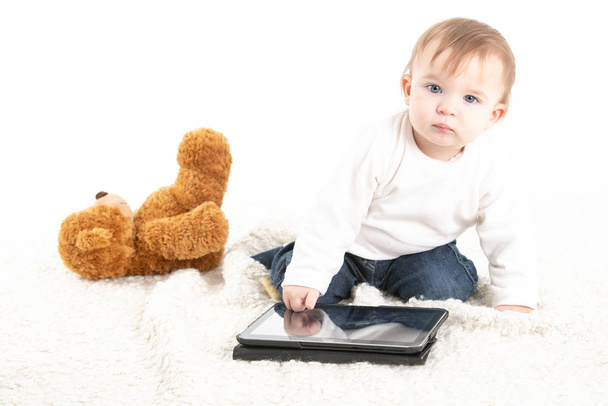 Bébé jouer avec une tablette et un ours en peluche en arrière-plan
 - Photo, image