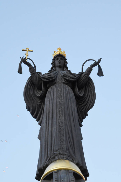 Posąg Katarzyny II na tle błękitnego nieba. W jednej ręce jest złoty krzyż, ręce otwarte na wszystkich. - Zdjęcie, obraz