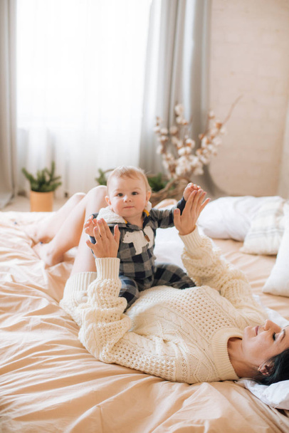 Young mother and little toddler son in a Scandinavian style bedroom decorated with Christmas garlands and needles on a large bright bed. Christmas mood - Fotó, kép