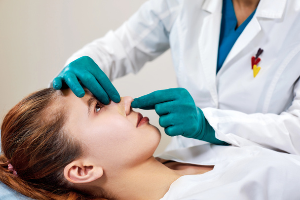 Женщина с гипсом на носу, врач осматривает лицо пациента после пластической операции
 - Фото, изображение