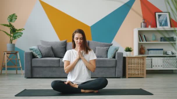 Attractive young woman in modern clothing exercising at home in lotus position - Felvétel, videó