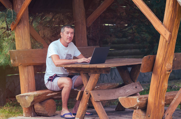 Young man working on a laptop in a wooden arbor on the nature - Photo, Image
