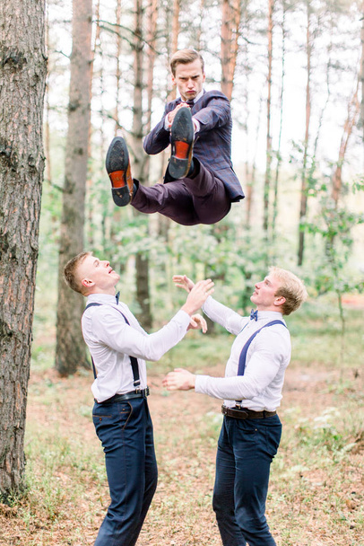 Handsome groom and groomsmen having fun and crazy in the forest while jumping on a wedding day. - Фото, зображення