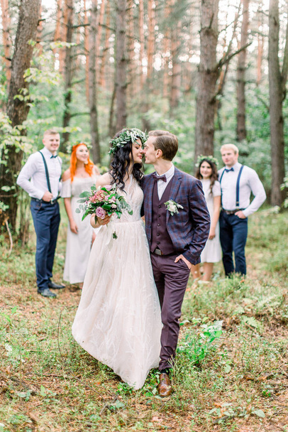 Kissing newlyweds stand in front of the couples of bridesmaids and groomsmen in the forest. Wedding in rustic style outdoors - Photo, Image