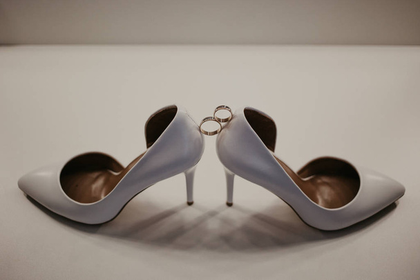 2 Két arany jegygyűrű két magas sarkú cipő között. Esküvői adatok az asztalon a tükör közelében - Fotó, kép