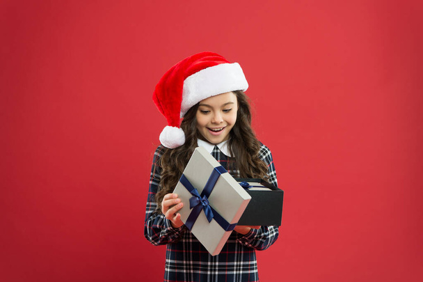 little girl open present box. happy new year gift. time for christmas holiday presents. small girl in santa hat. cheerful child red background. christmas kid shopping. best gift for xmas - Photo, image