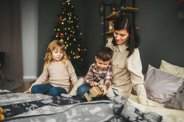 Мама зі своїми милими маленькими дітьми відкриває різдвяні подарунки в ліжку
. - Фото, зображення