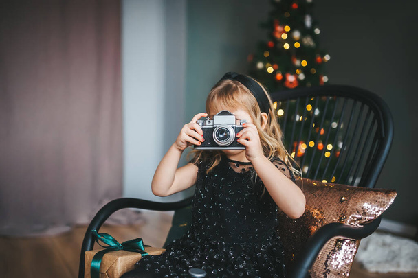 Little girl shooting photo with vintage camera near Christmas tree - Photo, Image