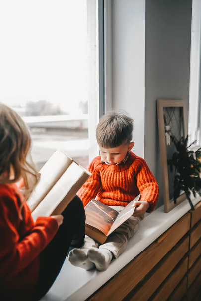 Enfants mignons lisant des livres sur le seuil près de la fenêtre
 - Photo, image