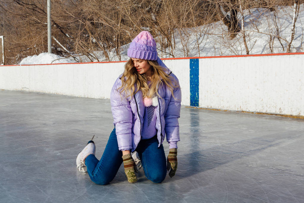 Lovely young woman sitting on the ice rink with ice skates on feet. - Foto, immagini