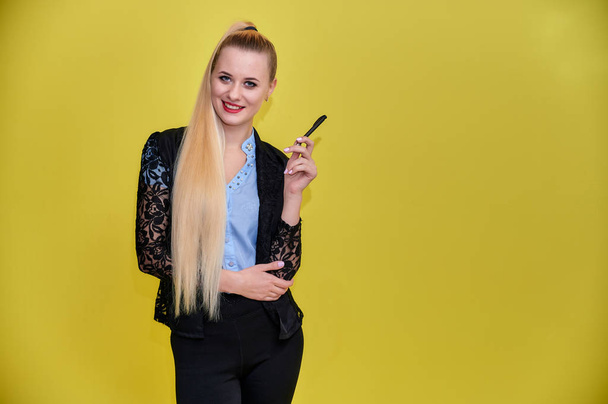 Portrait of a manager woman in a business suit with long beautiful hair and excellent make-up on a yellow background. Concept business blonde girl stands in front of the camera. - 写真・画像