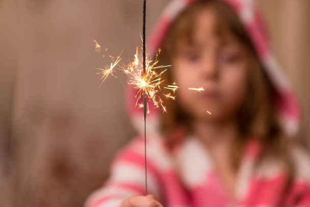 Happy small girl looking with admiration at burning sparkler in her hand over. - 写真・画像