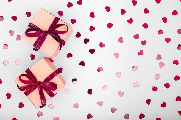 Ambachtelijke doos met donker rood fluwelen lint strik en glitter hart confetti. Valentijnsdag en milieuvriendelijk inpakconcept. Trendy minimalistische platte lay design achtergrond - Foto, afbeelding