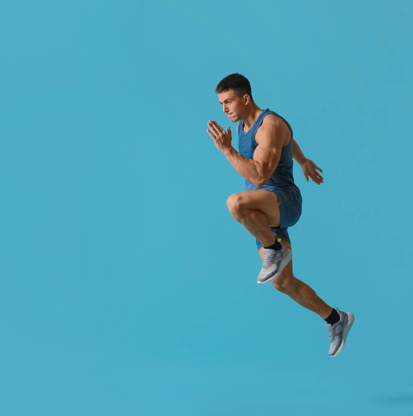 Athletic young man running on turquoise background, side view - Foto, Bild