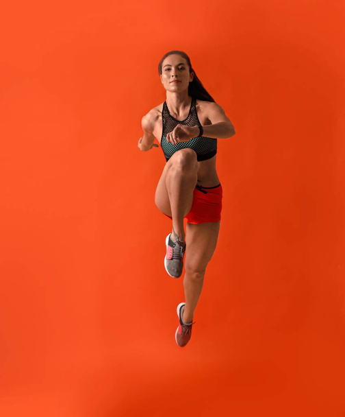 Athletic young woman running on red background - 写真・画像
