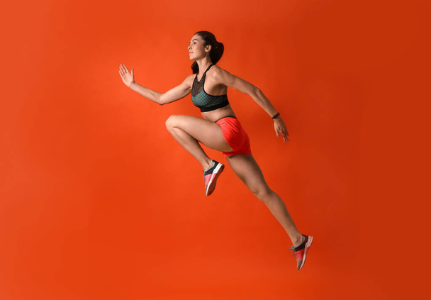 Athletic young woman running on red background, side view - Foto, Imagen