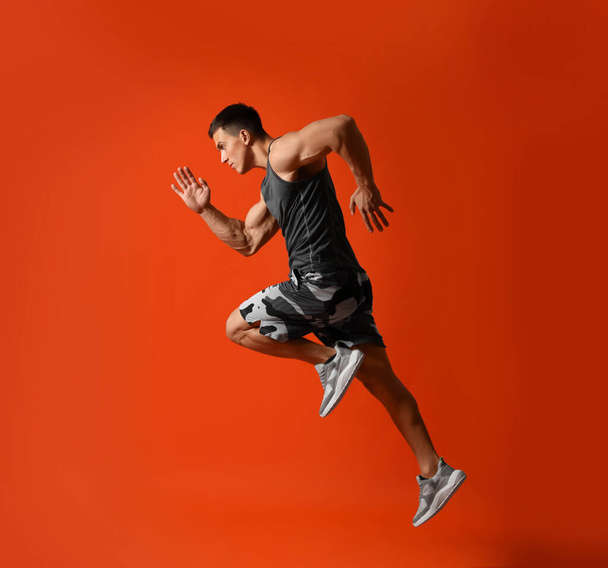 Atletický mladý muž běží na červeném pozadí, boční pohled - Fotografie, Obrázek