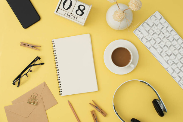 mordern Arbeitsplatz mit Tastatur, Kopfhörer, Kaffee, Glas, Telefon, Stift auf gelbem Hintergrund. Ansicht von oben, flach. - Foto, Bild