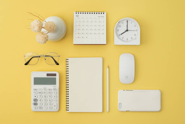 Notebook, mouse, phone, calculator, glasses, pen, calendar, alarm on yellow background. Flatlay, top view. - Photo, Image