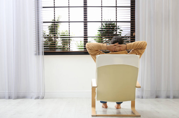 Man relaxing in armchair near window at home, back view. Space for text - Foto, Bild