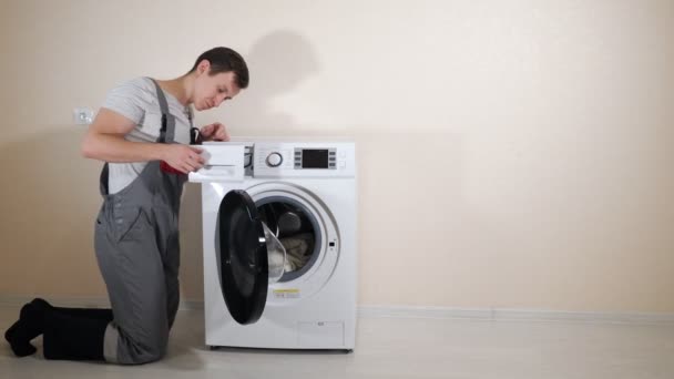 young serviceman in grey uniform repairs broken washing machine - Footage, Video