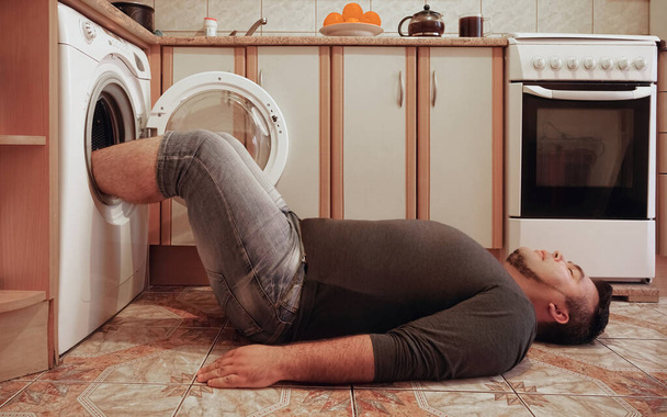 man on floor of kitchen. feet in centrifuge of washing machine. drying legs or socks.  - Fotoğraf, Görsel