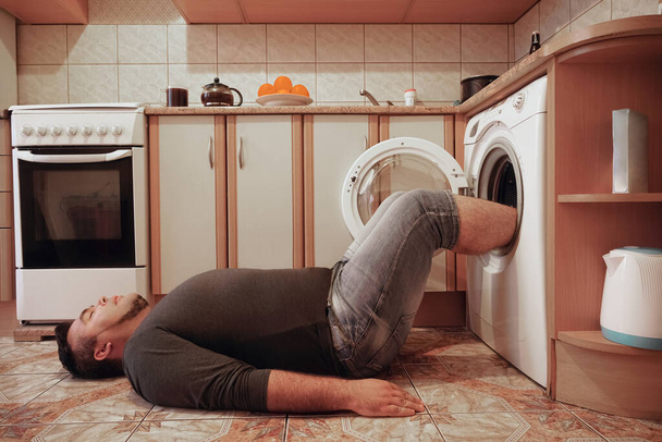 man on floor of kitchen. feet in centrifuge of washing machine. drying legs or socks.  - Foto, afbeelding