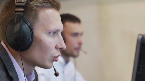 Male call center agent in wireless headset consulting online client. Using computer, business men operator talking working in customer service helpline support - Footage, Video