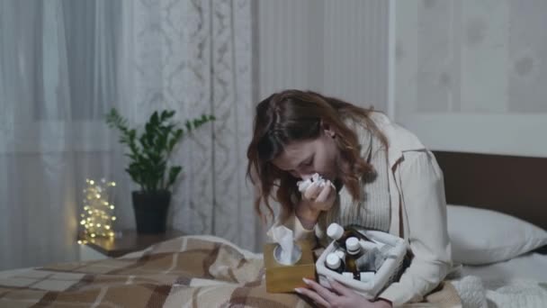 flu girl is sick coughs of a cold or flu suffers from high fever takes medication for common cold sitting sheltered by a warm blanket on sofa in room - Materiał filmowy, wideo