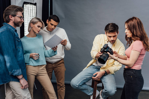 фотограф держит цифровую камеру рядом с красивой моделью и коллегами
  - Фото, изображение