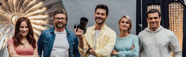panoramic shot of happy coworkers smiling while looking at camera in photo studio  - Photo, Image