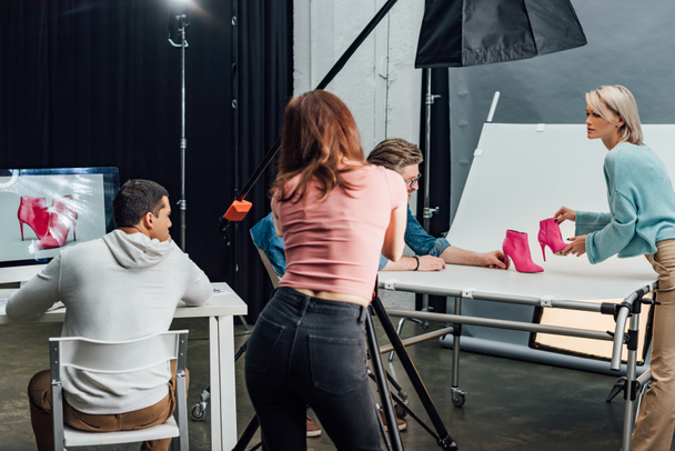 back view of photographer taking photo of pink shoes near coworkers in photo studio  - Foto, afbeelding