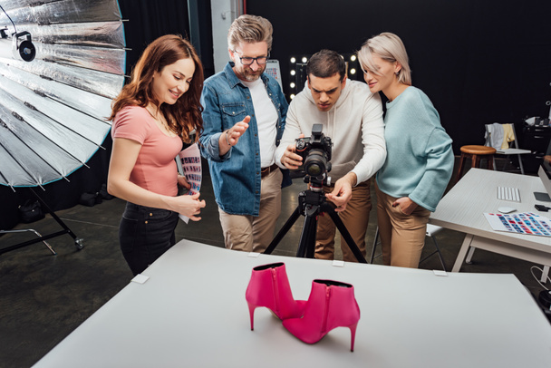 φωτογράφος φωτογραφία γυρίσματα ροζ παπούτσια κοντά ευτυχείς συναδέλφους στο στούντιο φωτογραφιών  - Φωτογραφία, εικόνα