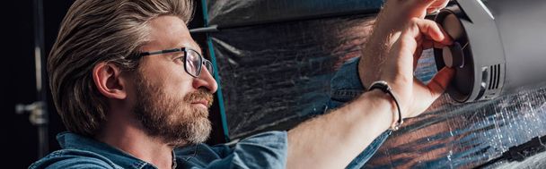 panoramic shot of bearded art director touching reflector in photo studio  - 写真・画像