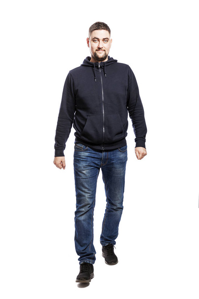 A handsome smiling young man in a hoodie and jeans is walking forward and looking at the camera. Full height. Isolated over white background.  - Foto, Imagem