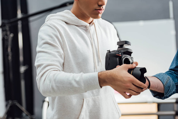 cropped view of photographer holding digital camera and taking camera lens  - Фото, зображення