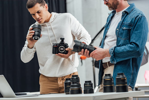 cropped view of bearded art director holding photo lens near photographer  - Foto, imagen