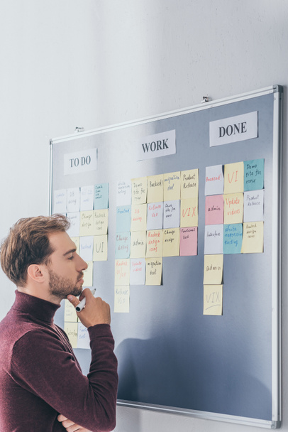 side view of handsome scrum master thinking near board with sticky notes and letters  - Photo, Image