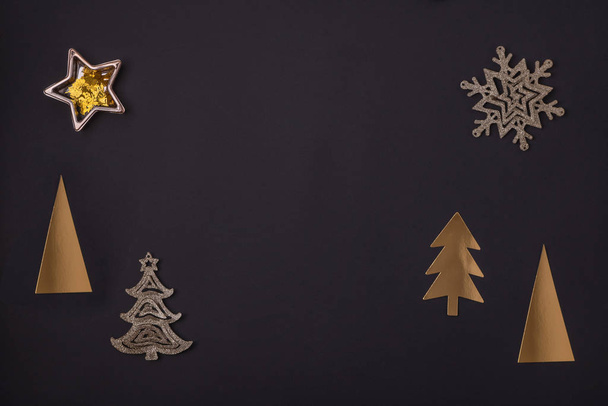 Sylwester i kartka świąteczna ze złotych świątecznych dekoracji - choinki, gwiazdy i płatki śniegu na czarnym tle. Widok z góry, płaski, przestrzeń do kopiowania - Zdjęcie, obraz
