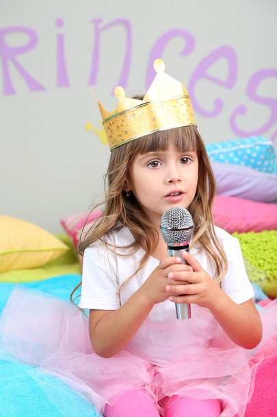 Little girl sitting on bed with microphone in room on grey wall background - Fotografie, Obrázek