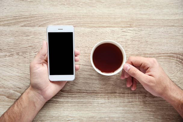 Man holding mobile phone and cup of tea - Photo, image