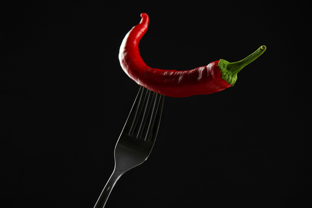 Red hot chili pepper on fork, isolated on black - Foto, Bild