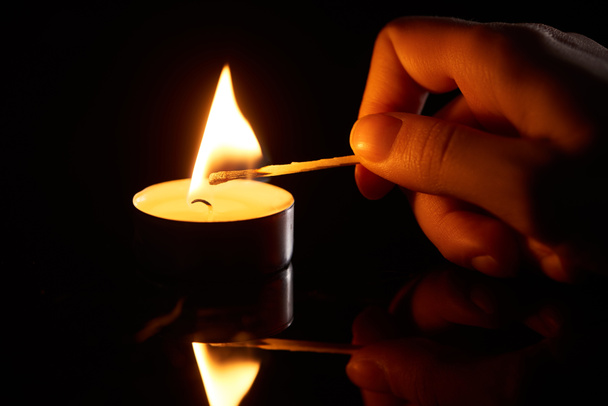 selective focus of woman lighting up candle with match isolated on black - Photo, Image